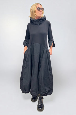 Avantgarde-Kleid in schwarz von Vincenzo Allocca aus Materialmix mit Memory-Stoff, Ballonrock, Kapuze, hochstellbarem Kragen und seitlichen Eingrifftaschen.

