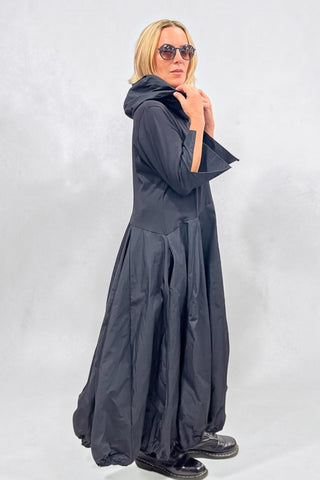 Avantgarde-Kleid in schwarz von Vincenzo Allocca aus Materialmix mit Memory-Stoff, Ballonrock, Kapuze, hochstellbarem Kragen und seitlichen Eingrifftaschen.
