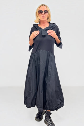 Avantgarde-Kleid in schwarz von Vincenzo Allocca aus Materialmix mit Memory-Stoff, Ballonrock, Kapuze, hochstellbarem Kragen und seitlichen Eingrifftaschen.
