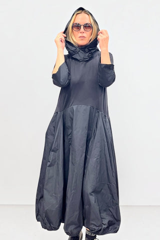 Avantgarde-Kleid in schwarz von Vincenzo Allocca aus Materialmix mit Memory-Stoff, Ballonrock, Kapuze, hochstellbarem Kragen und seitlichen Eingrifftaschen.
